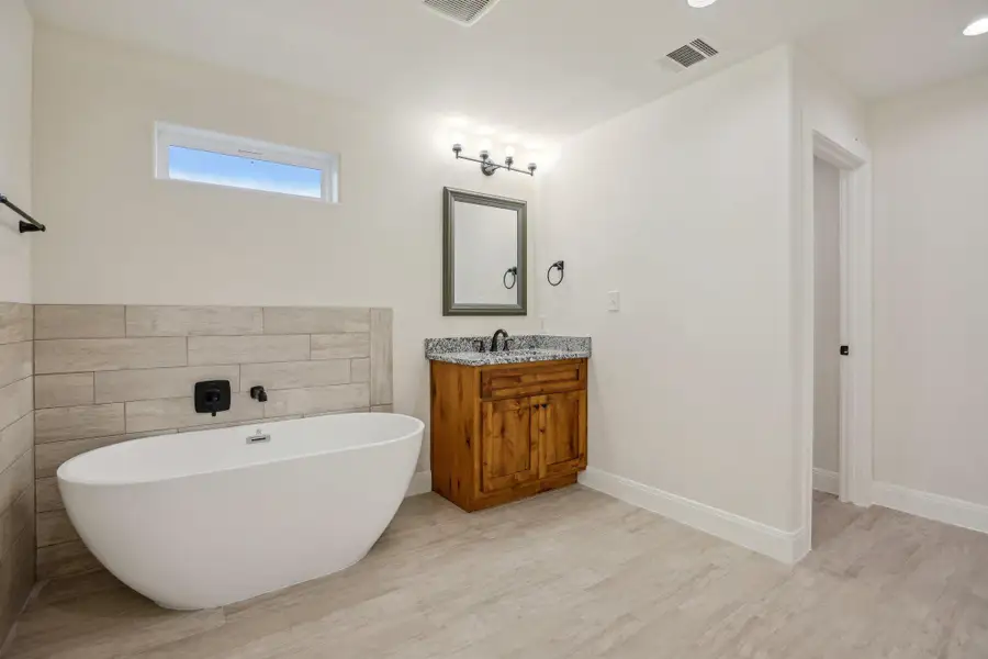 Primary Bathroom with a freestanding bath, wood finished floors, visible vents, vanity, and baseboards