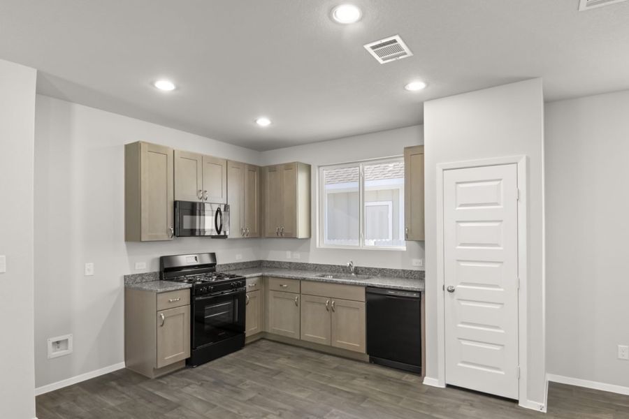 Image of a L-shaped kitchen with light brown cabinets, granite countertops, black appliances and a window above the sink