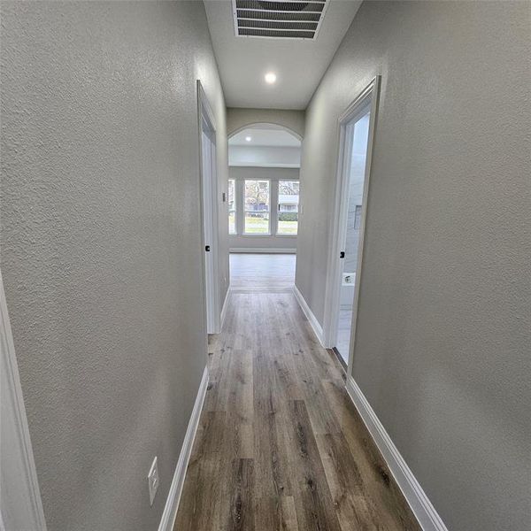 Hallway featuring a textured wall, light wood finished floors, recessed lighting, and arched walkways