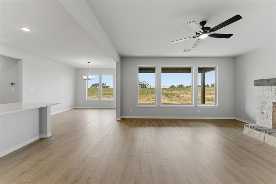 Unfurnished living room with a ceiling fan, light wood finished floors, suspended lighting, and a fireplace