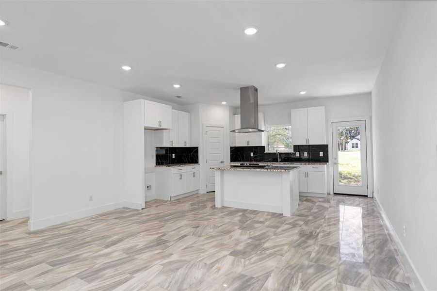 Kitchen with backsplash, white cabinets, a kitchen island, island range hood, and light stone counters