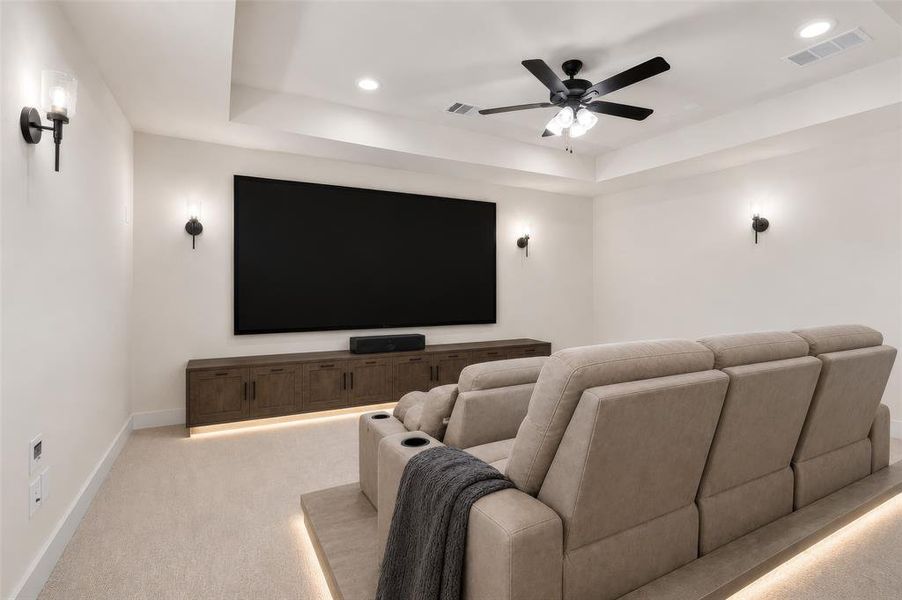 Dedicated media room featuring a large projection screen, tray ceiling, recessed lighting, and wall-mounted sconces