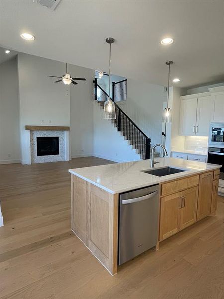 Kitchen featuring a fireplace, hanging light fixtures, open floor plan, a center island with sink, and stainless steel appliances