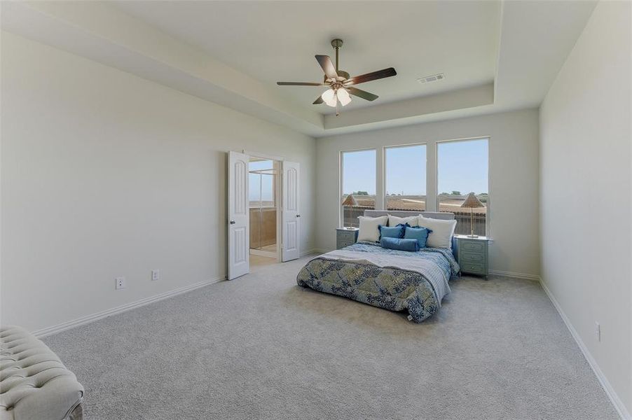 Spacious room featuring light gray carpeting, neutral wall finishes, a tray ceiling with a ceiling fan, and three large windows