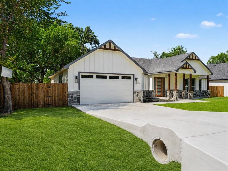 Modern ranch-style home featuring white board and batten siding, dark stone accents, wood-look porch columns, a gray shingled roof, and a concrete driveway Modern ranch-style home featuring white board and batten siding, dark stone accents, wood-look porch columns, a gray shingled roof, and a concrete driveway