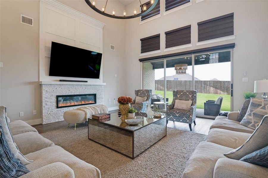 Spacious living area featuring a stone-faced fireplace with an electric insert, high ceilings, wood-finish flooring, and expansive glass sliding doors