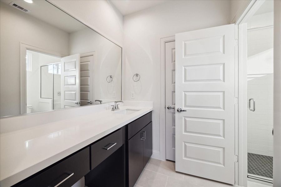 This sleek first-floor bathroom features a large vanity with plenty of counter space and dark cabinetry for a modern, elegant look.
