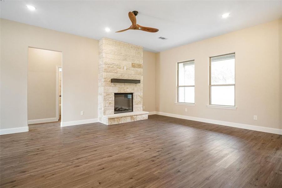 Unfurnished living room featuring dark hardwood / wood-style floors, ceiling fan, and a stone fireplace