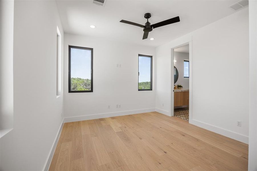 Luminous bedroom #3 room features pristine wood flooring, clean white walls, and a modern ceiling fan.