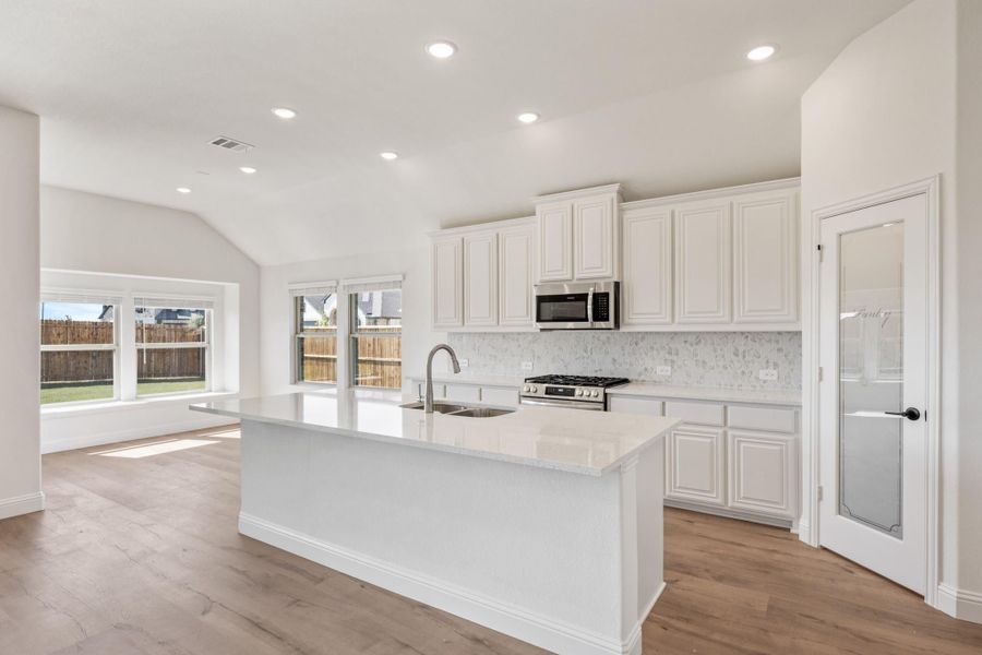 Open kitchen with white cabinets, large island, quartz countertops, and stainless steel appliances on wood floors Open kitchen with white cabinets, large island, quartz countertops, and stainless steel appliances on wood floors