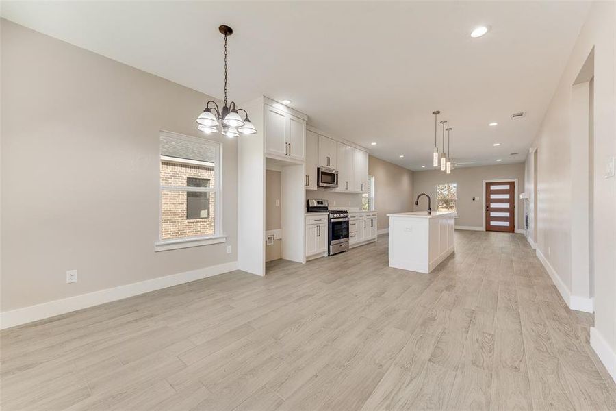 Kitchen with appliances with stainless steel finishes, an island with sink, white cabinets, hanging light fixtures, and light hardwood / wood-style floors