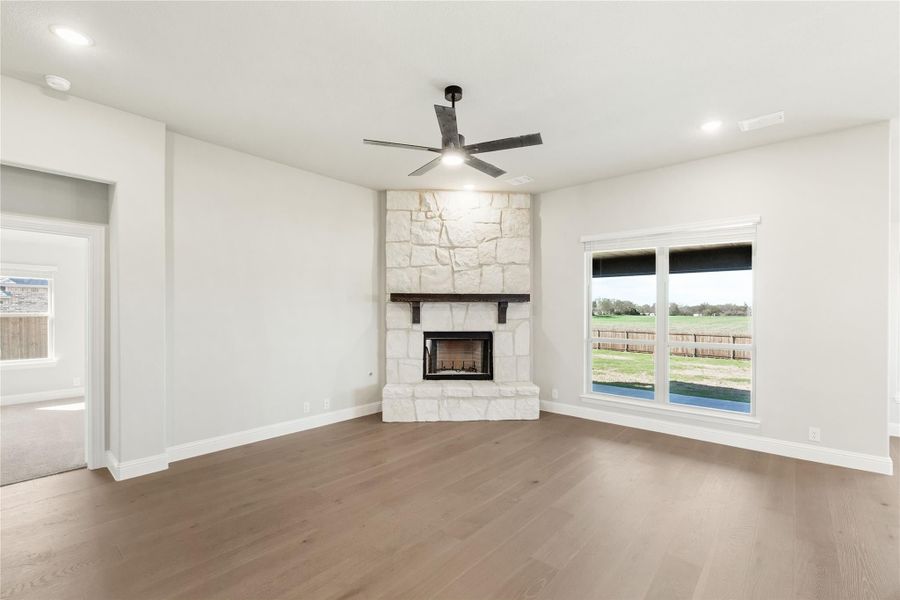 Living room with corner stone fireplace, hardwood floors, and ceiling fan Living room with corner stone fireplace, hardwood floors, and ceiling fan