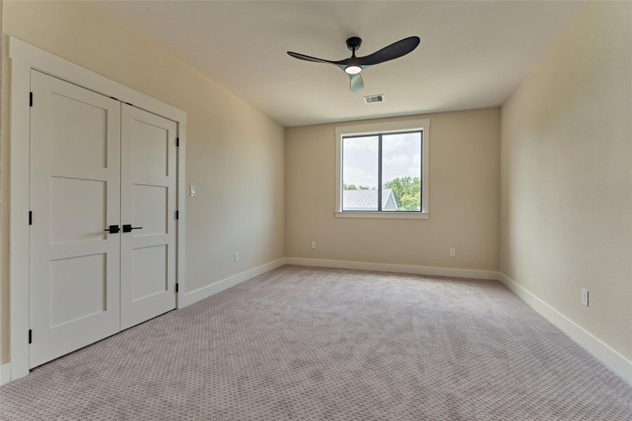 Spacious secondary bedroom with plush carpet, a double-door closet, a large window with a metal-roof and treetop view, and a modern ceiling fan — comfortable, private, and full of surprises. Spacious secondary bedroom with plush carpet, a double-door closet, a large window with a metal-roof and treetop view, and a modern ceiling fan — comfortable, private, and full of surprises.