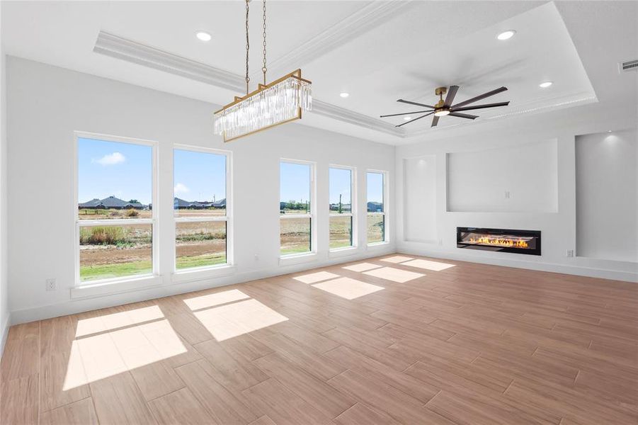 Unfurnished living room featuring a raised ceiling, a glass covered fireplace, light wood-type flooring, ceiling fan, and recessed lighting Unfurnished living room featuring a raised ceiling, a glass covered fireplace, light wood-type flooring, ceiling fan, and recessed lighting