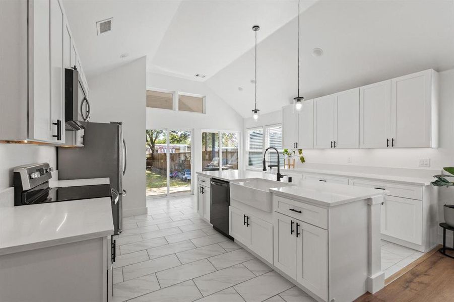 Kitchen featuring a kitchen island with sink, white cabinetry, high vaulted ceiling, decorative light fixtures, and appliances with stainless steel finishes