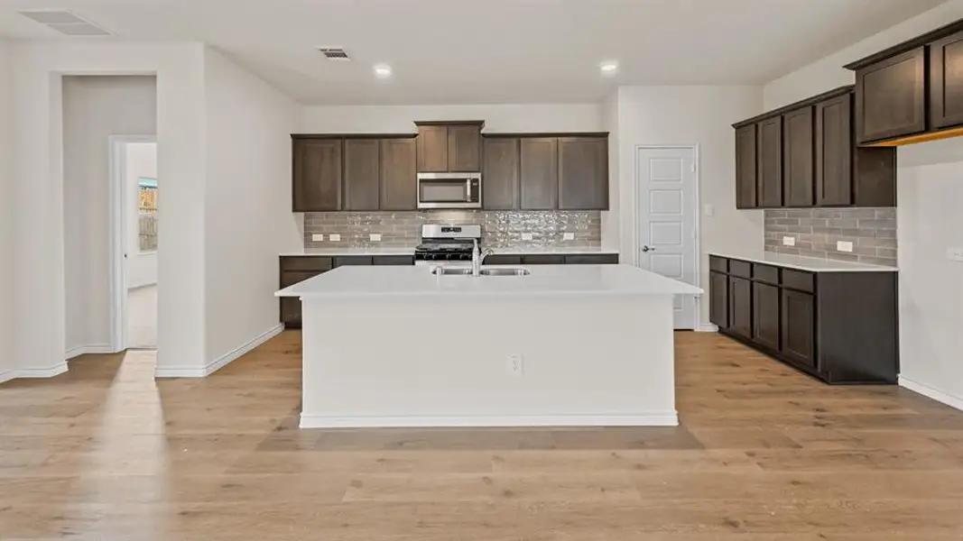 Contemporary kitchen featuring a large central island, dark wood-finish cabinetry, light-toned countertops, and a subway tile backsplash Contemporary kitchen featuring a large central island, dark wood-finish cabinetry, light-toned countertops, and a subway tile backsplash