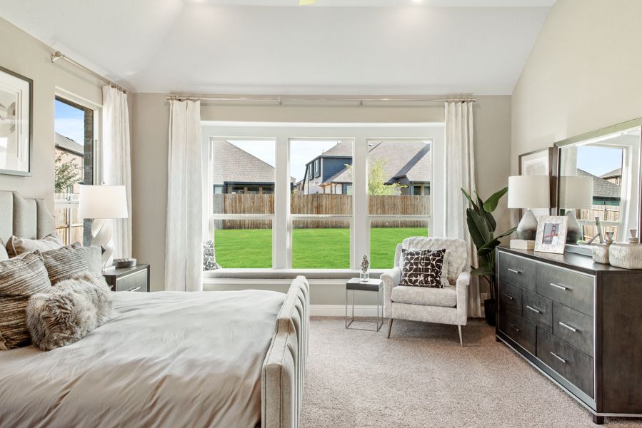 Master bedroom with vaulted ceiling, large bay window overlooking backyard, carpet floors, and dark wood dresser
