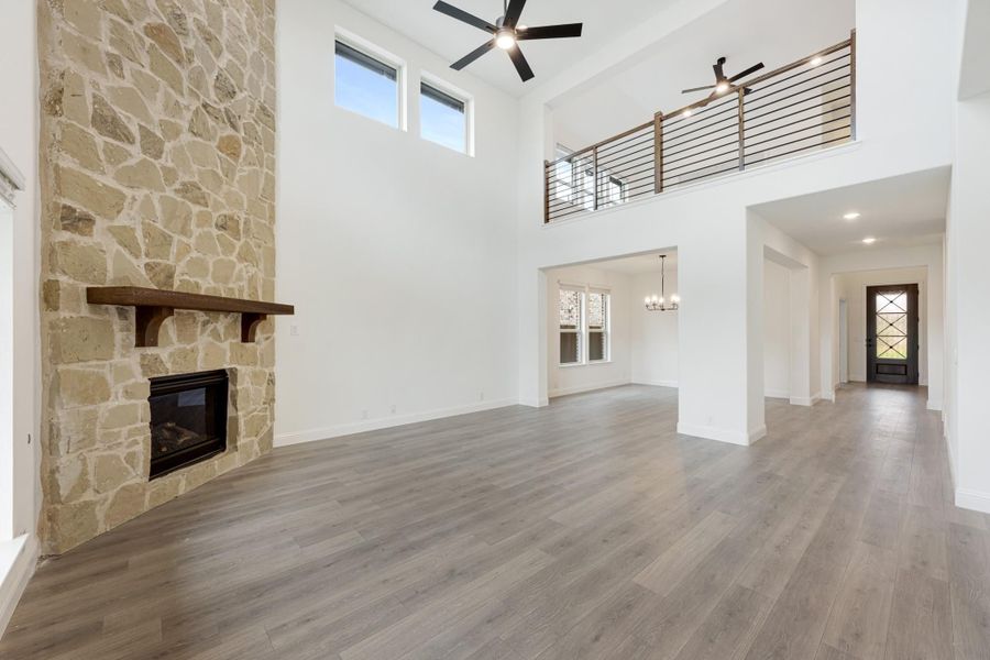 Open living room with two-story ceiling, floor-to-ceiling stone fireplace, wood floors, and upper balcony railing Open living room with two-story ceiling, floor-to-ceiling stone fireplace, wood floors, and upper balcony railing