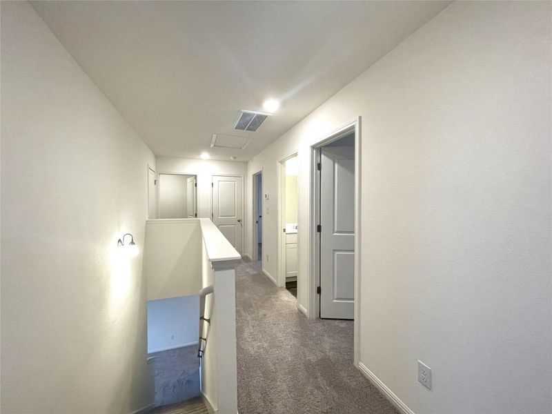 Hallway with visible vents, an upstairs landing, baseboards, and dark carpet