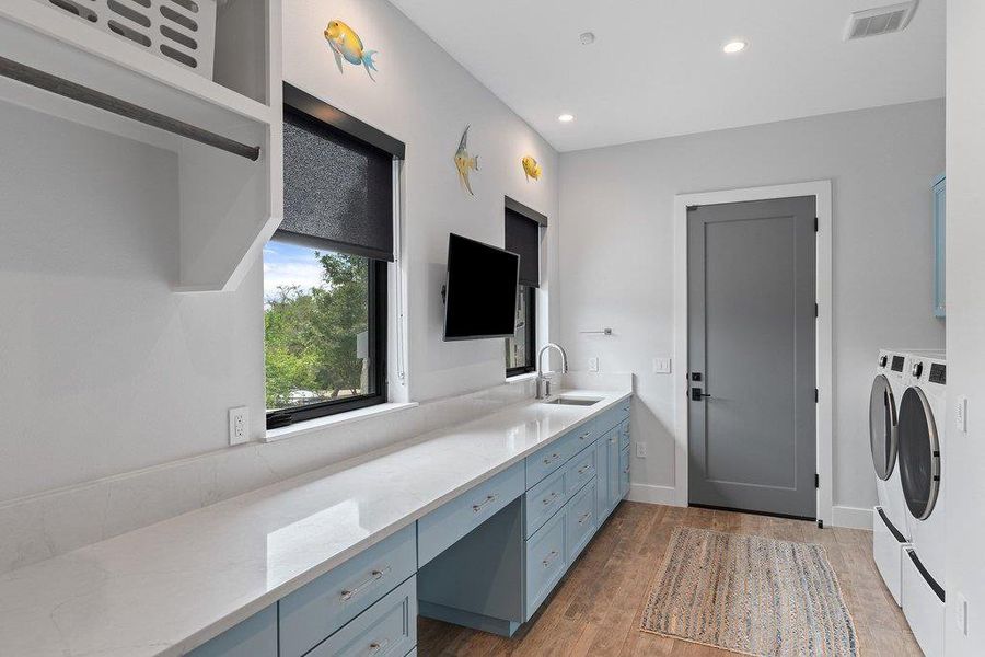 The spacious laundry room offers extensive counter space for folding and organization, paired with custom cabinetry in a soft blue hue and integrated hanging rods for maximum efficiency.