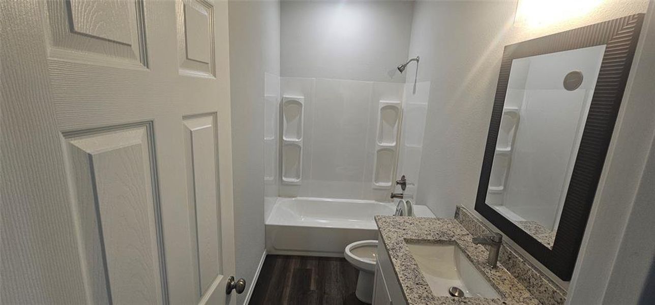 Bathroom with  shower combination, dark wood finished floors, vanity, and a textured wall