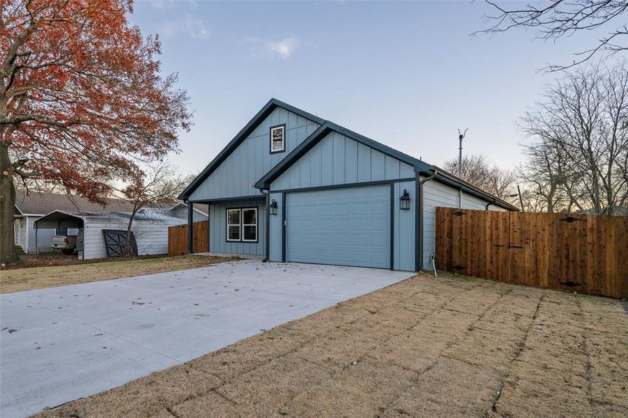 View of front of house with concrete driveway, board and batten siding, a gate, and an attached garage