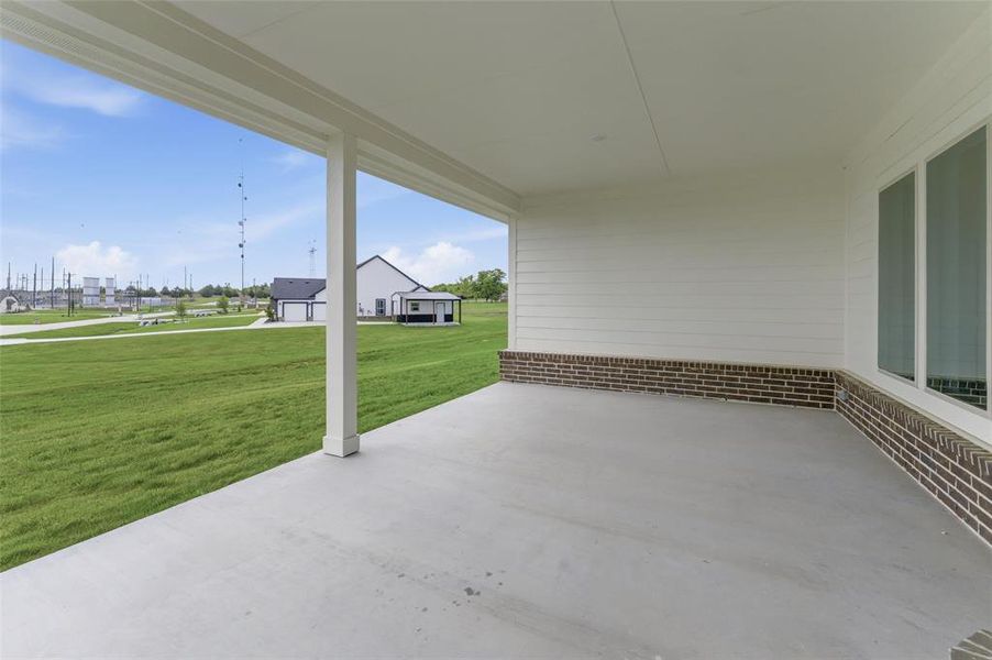 The property features a covered patio with a concrete surface and white pillars, overlooking an expansive green lawn