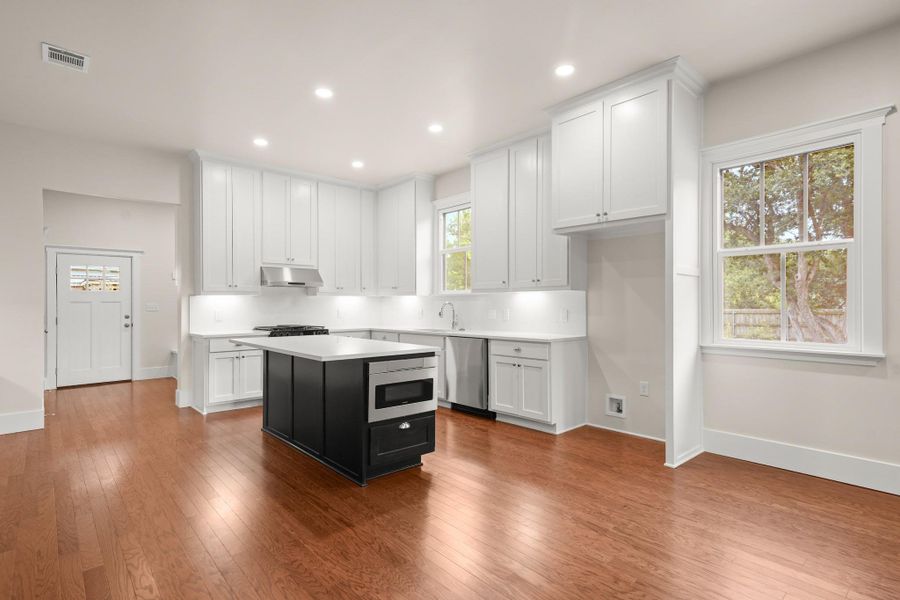 A well-lit culinary space showcases an island with integrated appliances and warm hardwood floors. A well-lit culinary space showcases an island with integrated appliances and warm hardwood floors.