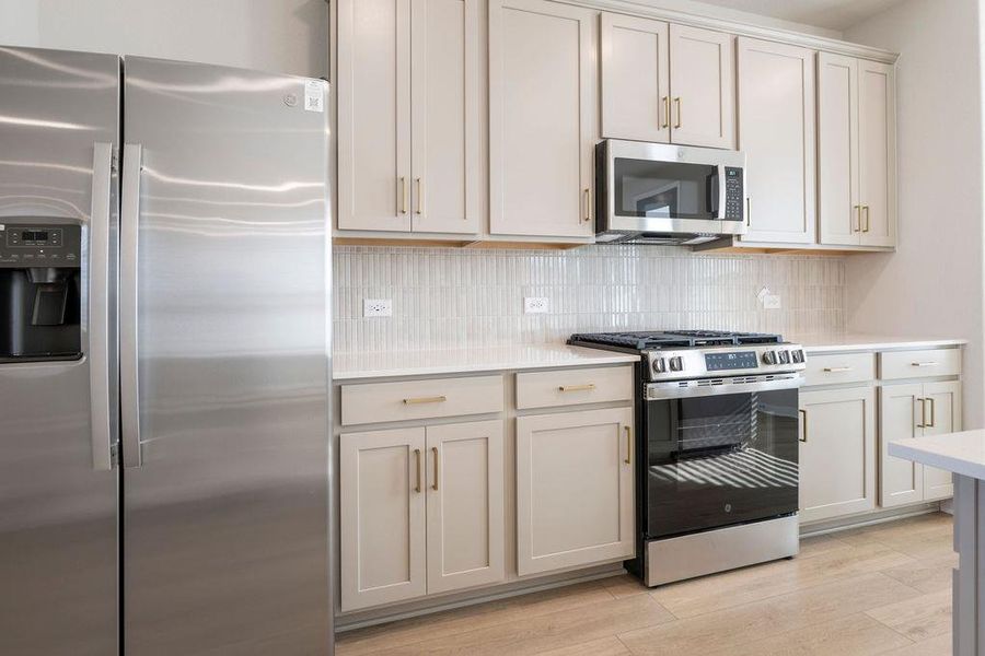 Kitchen featuring stainless steel appliances, tasteful backsplash, light wood-style flooring, light stone counters, and cream cabinetry