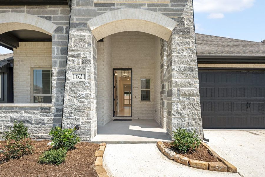 Home entrance with arched stone surround, black front door, and address number 1621 visible on brick exterior.