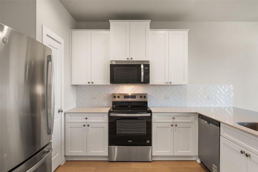Kitchen featuring stainless steel appliances, white cabinets, and light stone counters Kitchen featuring stainless steel appliances, white cabinets, and light stone counters
