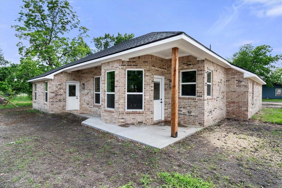 Brick exterior featuring a covered patio with a wood support post, multiple windows, and a dark shingle roof