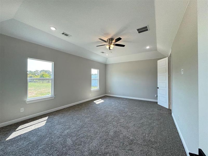 Spacious room featuring tray ceilings, recessed lighting, a ceiling fan, two windows, and dark gray carpeting
