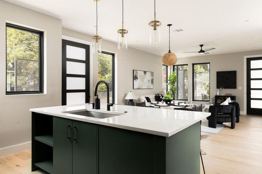 Kitchen featuring green cabinets, a kitchen island with sink, light wood-style floors, and hanging light fixtures