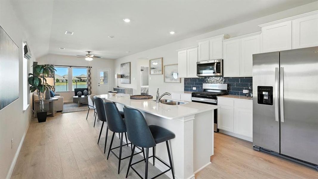 Kitchen with stainless steel appliances, decorative backsplash, a kitchen island with sink, white cabinets, and recessed lighting