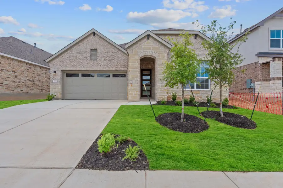 View of front of home featuring stone siding, a garage, driveway, and a front yard View of front of home featuring stone siding, a garage, driveway, and a front yard