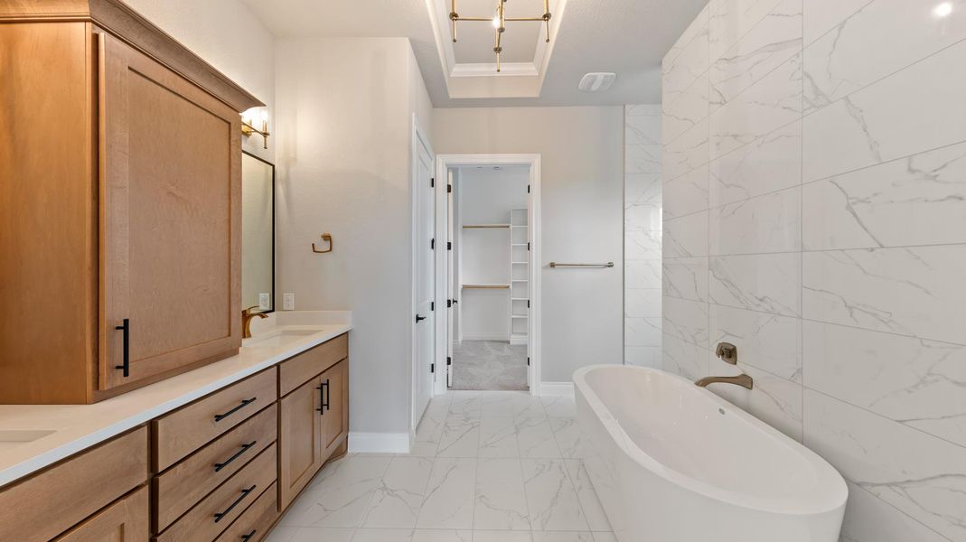 Bathroom featuring a spacious closet, a freestanding tub, tile walls, and light marble finish flooring