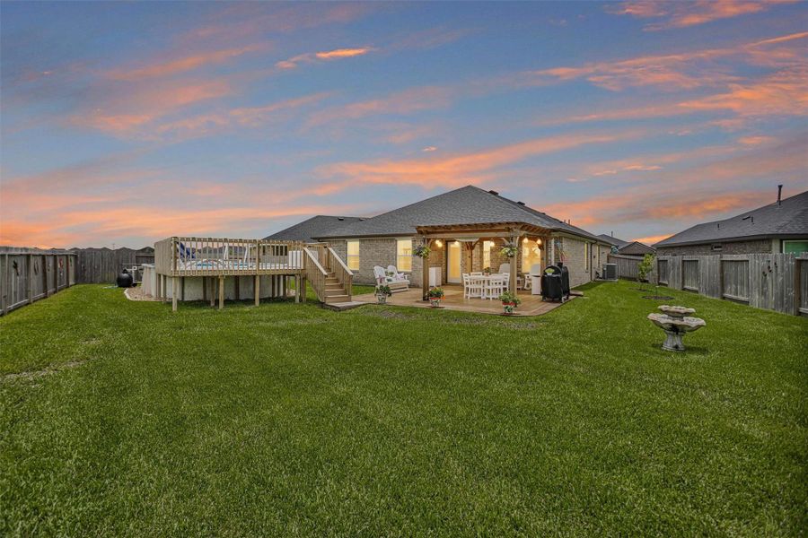 Spacious backyard with a well-maintained lawn, featuring a wooden deck with a pool and a charming covered patio area perfect for outdoor dining and relaxation.