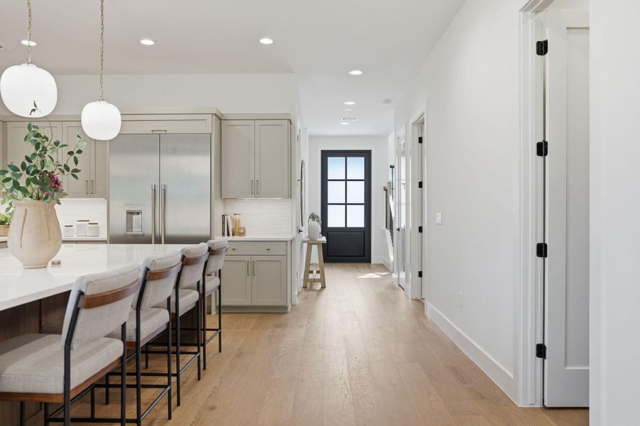 Kitchen featuring light wood-style floors, stainless steel built in fridge, a breakfast bar, decorative light fixtures, and decorative backsplash