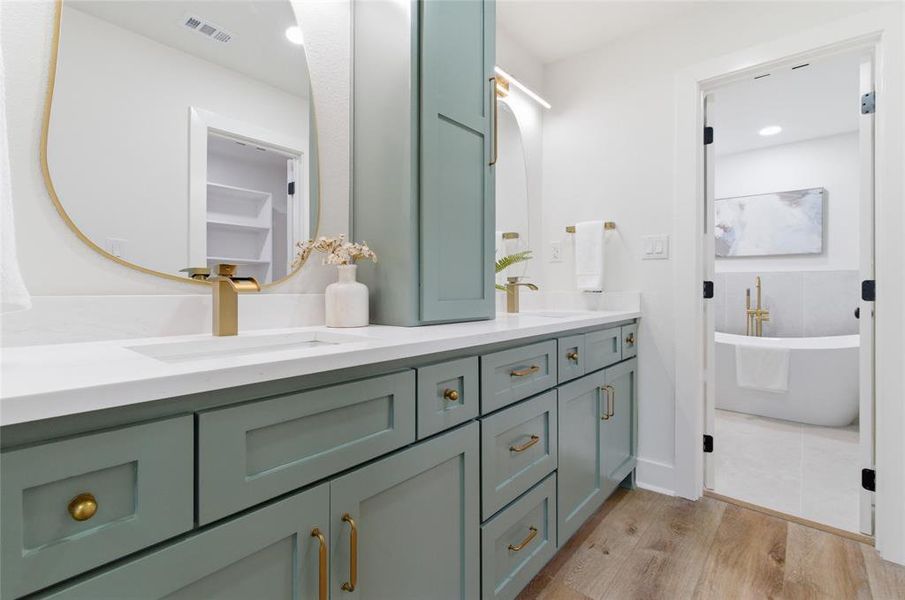 Bathroom vanity featuring light green cabinetry with gold hardware, a white countertop, and dual sinks with gold fixtures Bathroom vanity featuring light green cabinetry with gold hardware, a white countertop, and dual sinks with gold fixtures