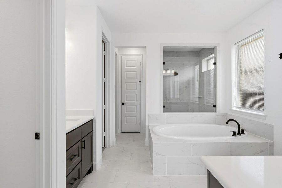 Experience luxury in this expansive primary bathroom, complete with a stunning garden tub, walk in shower, sleek quartz countertops, and contemporary tile accents—a perfect oasis for relaxation and rejuvenation.