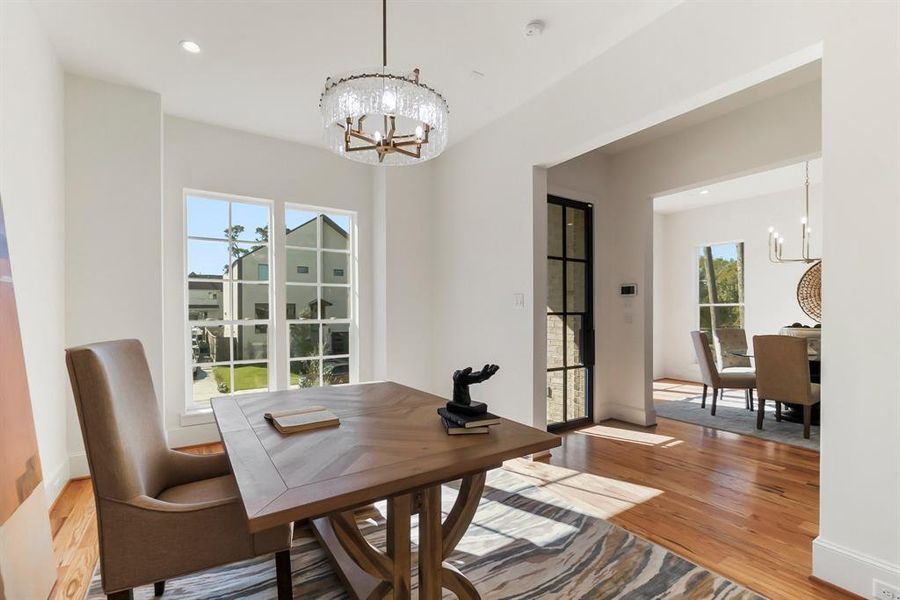 Elegant home office with natural light streaming through large windows, warm wood flooring, and a seamless flow to the dining area.