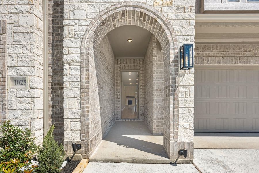 Brick arched entryway leading to front door with wall sconce and garage door visible beside it Brick arched entryway leading to front door with wall sconce and garage door visible beside it