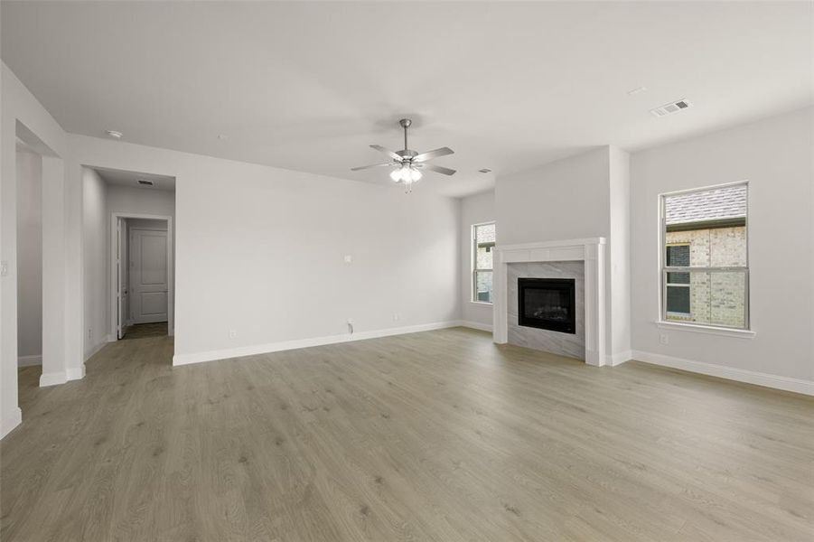 Unfurnished living room featuring ceiling fan, light wood-type flooring, and a premium fireplace Unfurnished living room featuring ceiling fan, light wood-type flooring, and a premium fireplace