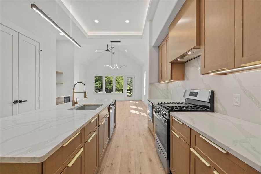 Kitchen with light stone counters, stainless steel appliances, light wood finished floors, a large island with sink, and pendant lighting