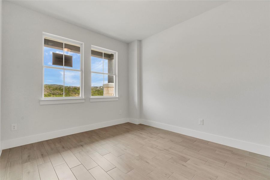A naturally illuminated room features light wood flooring and hillside views from twin windows.