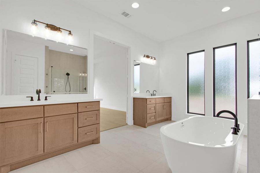 Primary Bathroom with two vanities, a freestanding tub, a large shower stall with bench seat, recessed lighting, and light tile patterned floors
