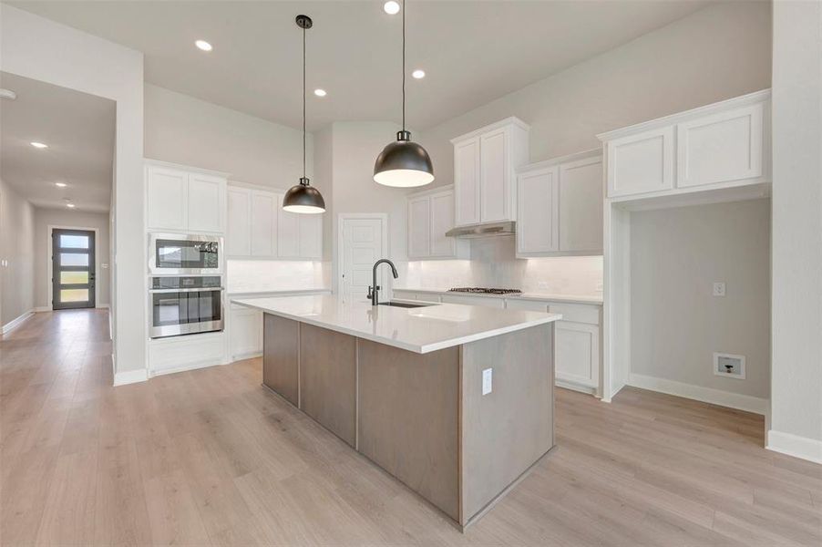 Open-concept kitchen featuring a central island with a sink, white cabinetry, integrated stainless steel appliances, and wood-finish flooring