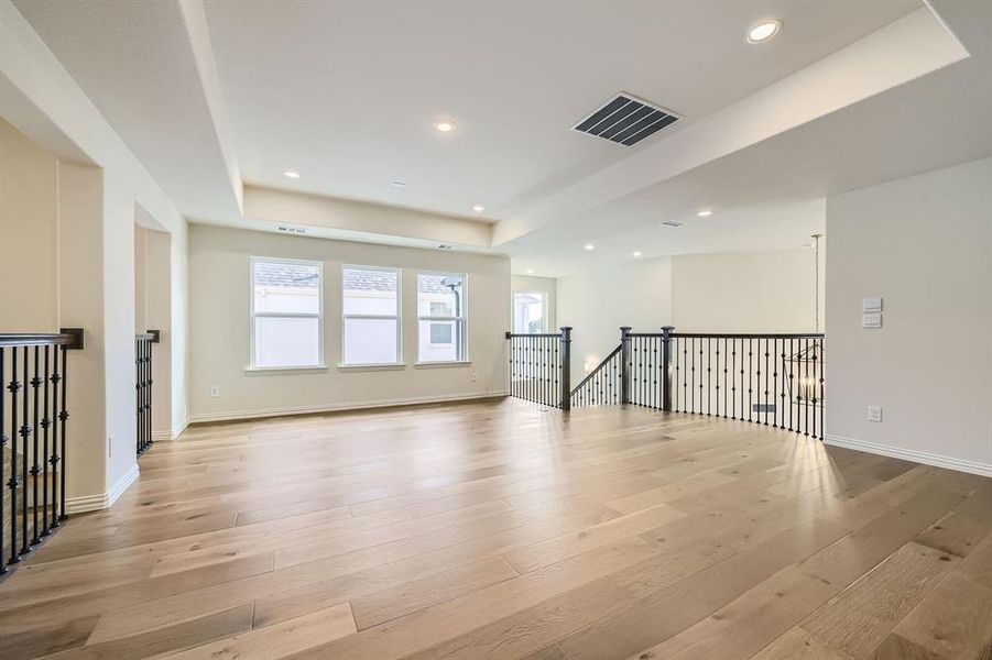 Game room with light hardwood / wood-style flooring, iron railing and a tray ceiling