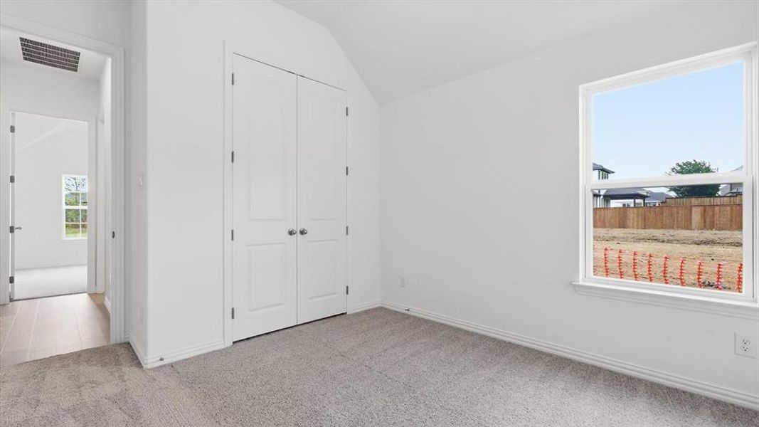 Vaulted ceiling room with an expansive window, light-toned carpeting, and a double-door closet Vaulted ceiling room with an expansive window, light-toned carpeting, and a double-door closet